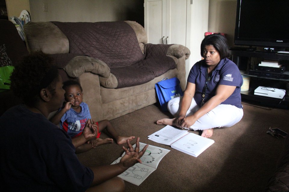 Yamika McCalpine, a home visitor with Health Families, sits on the floor in Monica Gadson’s house.