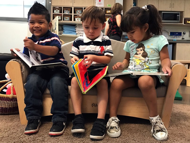 Educare Arizona classmates Nathan Jaramillo, far left, Esteban Cuevas and Melissa Gordillo “read” books during free time in their toddler classroom. Children begin learning basic literacy skills, like which direction to turn the pages, around age 2. Lillian Mongeau/The Hechinger Report