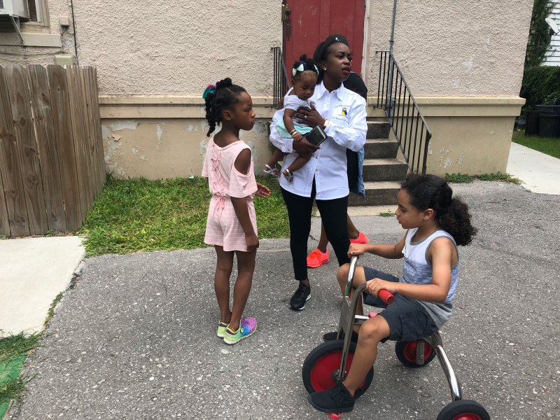 School founder Vera Triplett holds a potential future student while chatting with current students Joelia Simmons and Langston Kali.